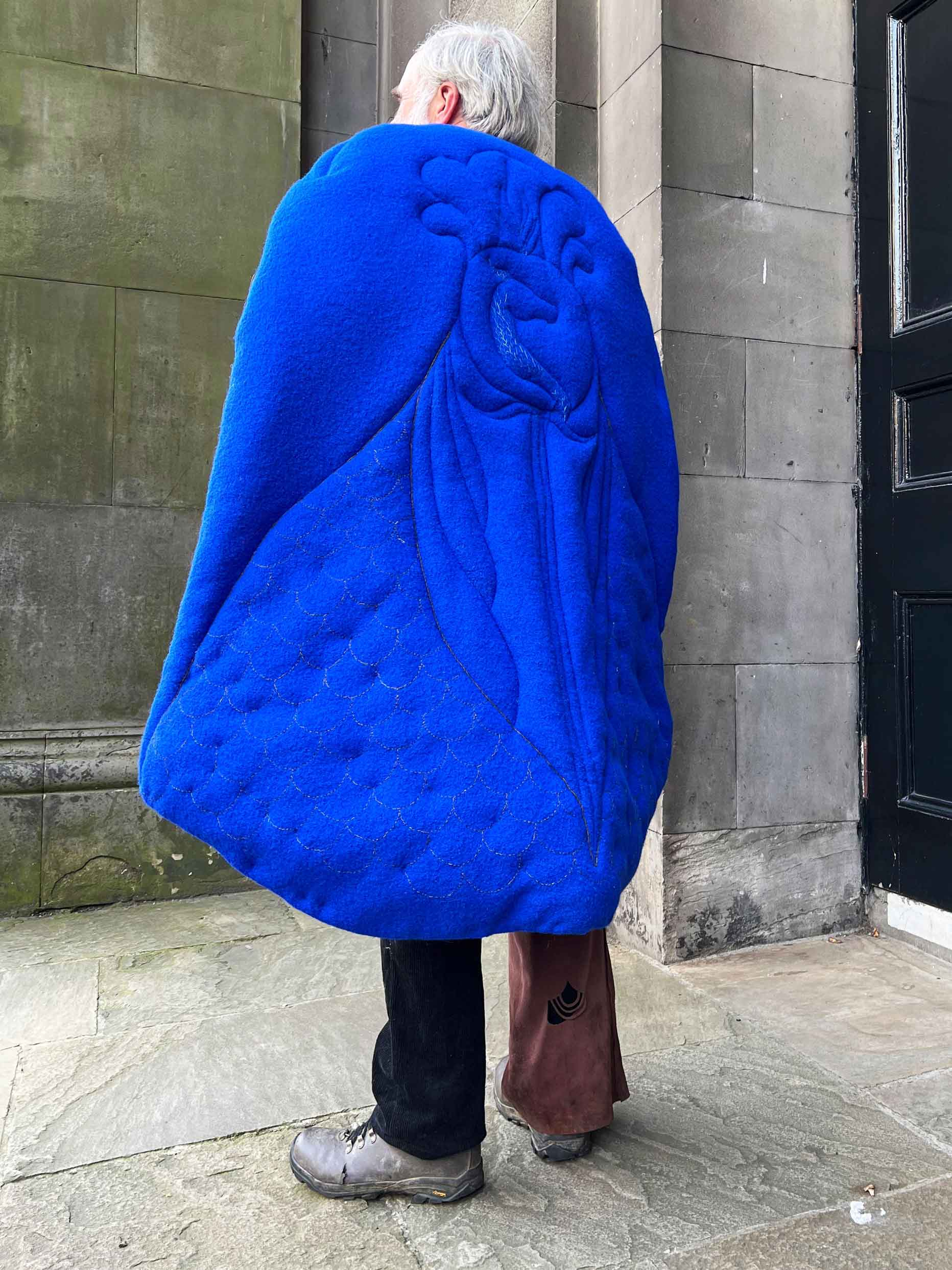 A blue cape that is quilted with a dragon head, and embroidered with scales