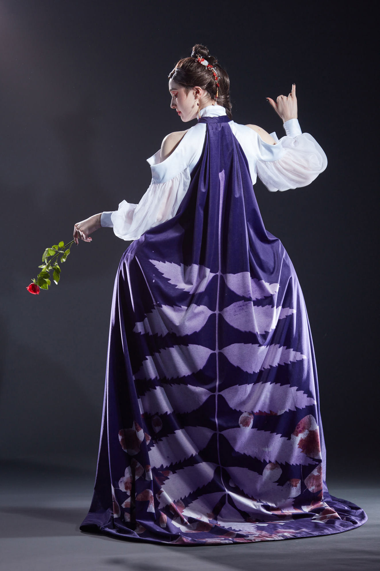 The costume created for the character Lacie from Pandora Hearts. The model wears a purple dress with a red corset, white skirt and sleeves. 