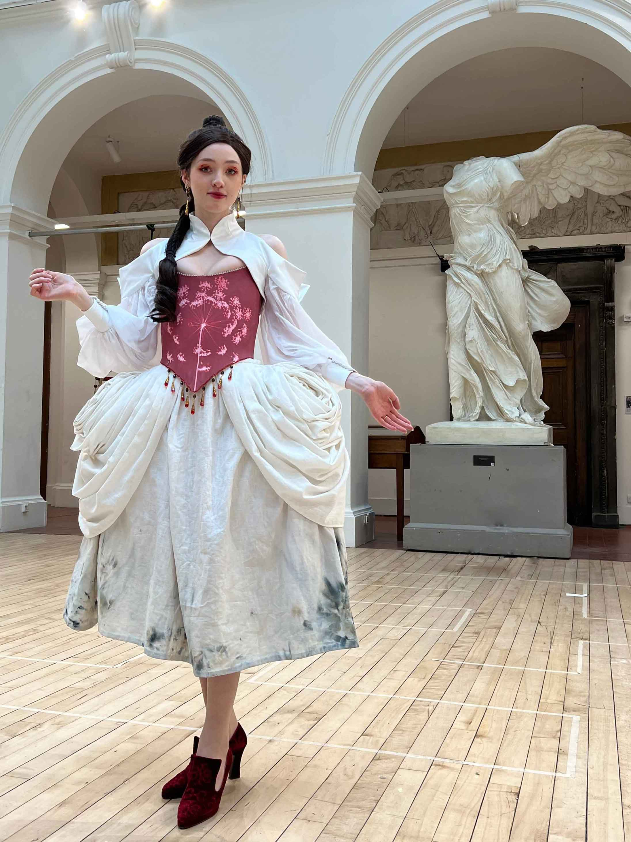 The costume created for the character Lacie from Pandora Hearts. The a red corset, white skirt and sleeves. Her brown braid sits over her shoulder